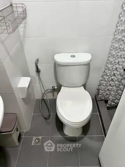 Modern bathroom with sleek white toilet and gray tile flooring, featuring a handheld bidet spray.