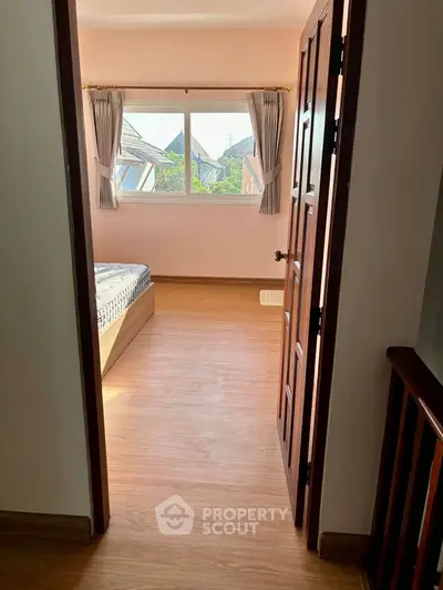 Bright bedroom with wooden flooring and large window offering natural light.