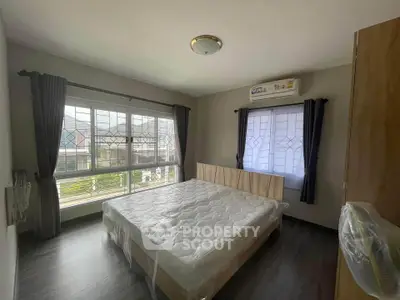 Spacious bedroom with large windows allowing ample natural light, featuring a comfortable bed and wooden flooring.