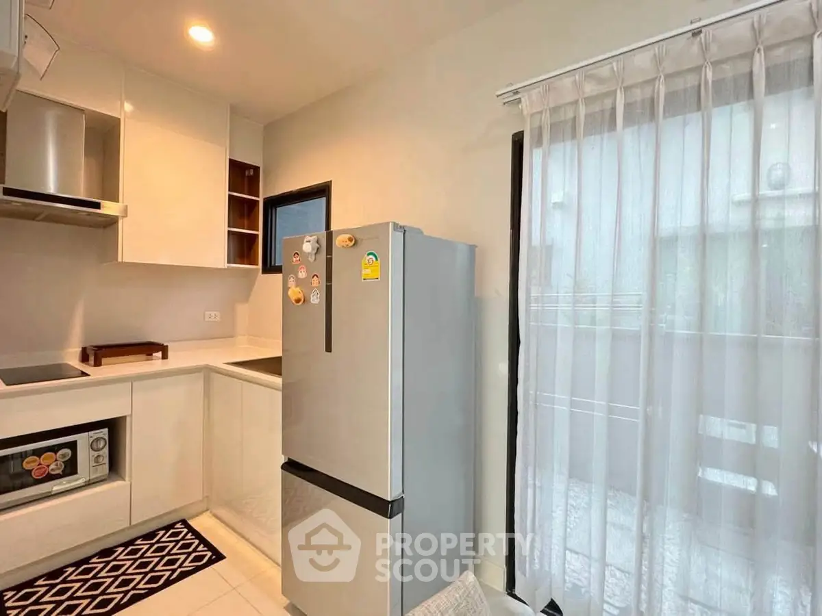 Modern kitchen with sleek fridge and ample natural light through sheer curtains.