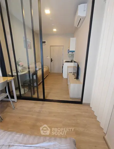Modern studio apartment with glass partition, cozy living area, and compact kitchen.