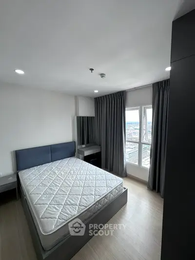 Modern bedroom with large window and city view, featuring a comfortable bed and sleek furnishings.