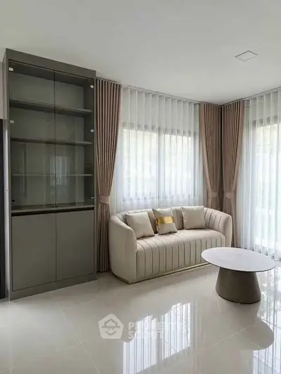 Elegant living room with modern sofa and glass cabinet, featuring floor-to-ceiling windows and stylish curtains.