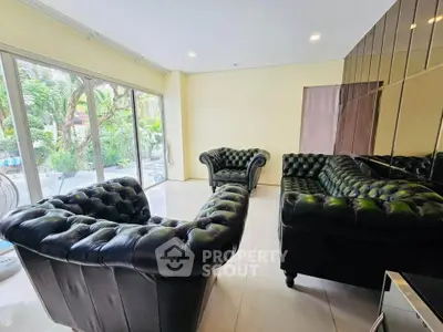 Spacious living room with elegant leather sofas and large windows overlooking a lush garden.
