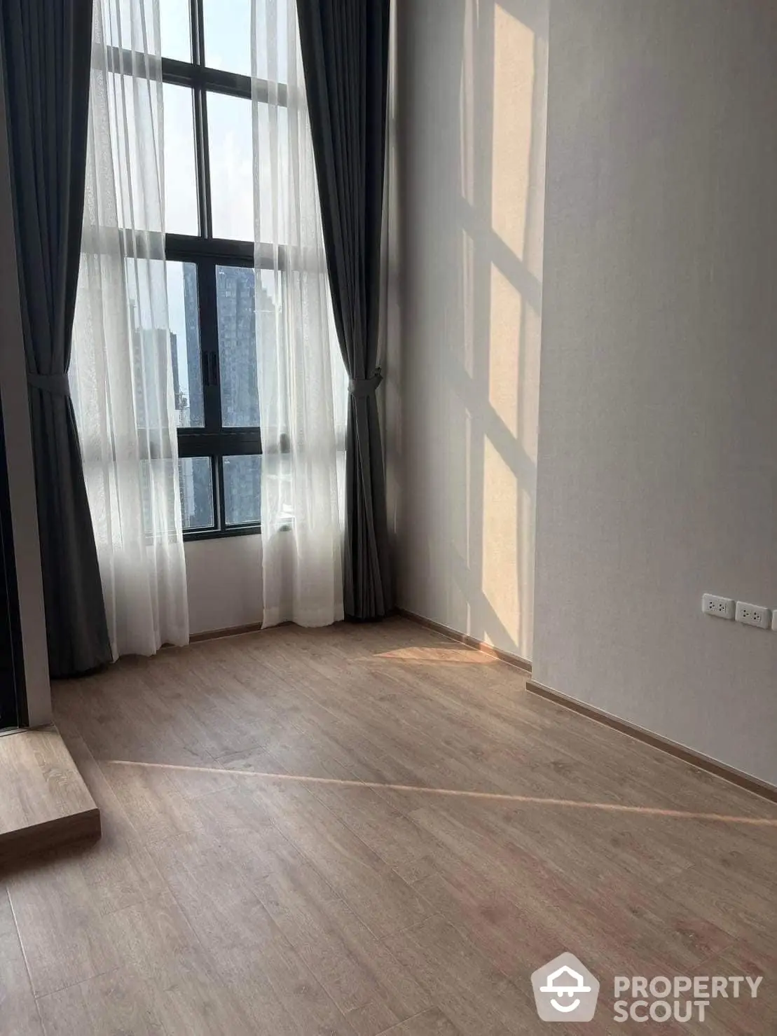 Spacious and well-lit corner unit with large windows draped in sheer curtains, offering a blend of privacy and natural light, perfect for a serene living room setup.