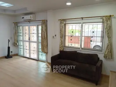 Spacious living room with large windows and elegant curtains, featuring a cozy sofa and wooden flooring.