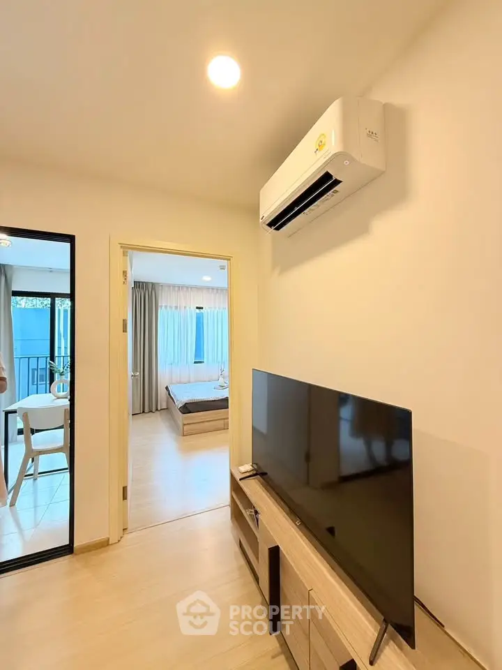 Modern apartment interior with sleek TV setup and air conditioning, leading to a cozy bedroom with natural light.