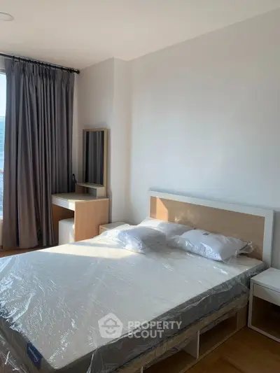 Modern bedroom with natural light, featuring a bed, nightstand, and dressing table, ideal for urban living.