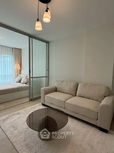 Modern living room with cozy beige sofa and glass coffee table, adjacent to a stylish bedroom.