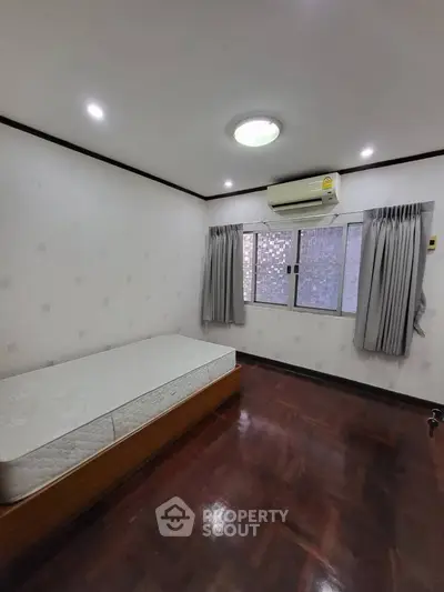 Spacious bedroom with wooden flooring and air conditioning in modern apartment.