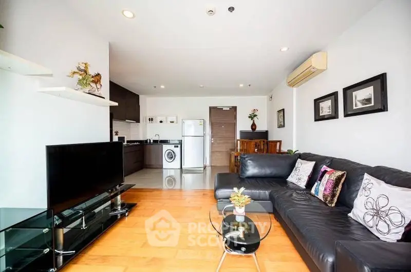 Spacious modern living room with sleek black leather sofa and open kitchen layout.