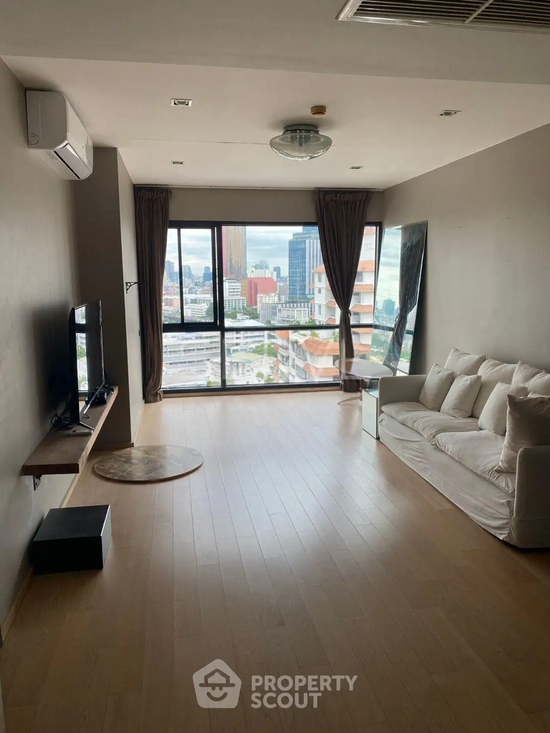 Spacious living room with city view, modern furnishings, and large windows in a high-rise apartment.