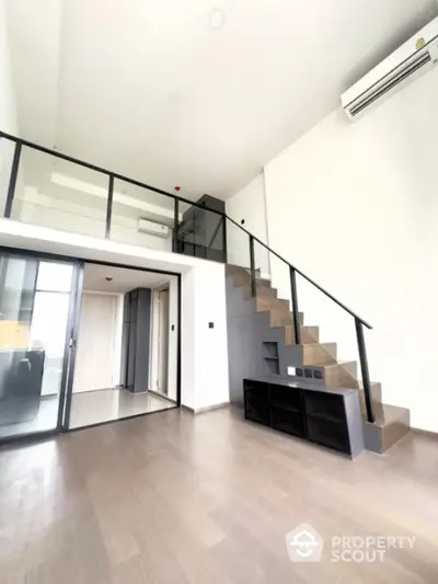 Modern duplex apartment with sleek staircase and glass railing, featuring high ceilings and minimalist design.