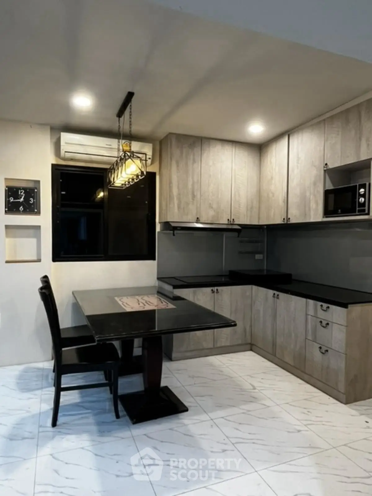 Modern kitchen with sleek cabinetry and dining area, featuring stylish lighting and tiled flooring.