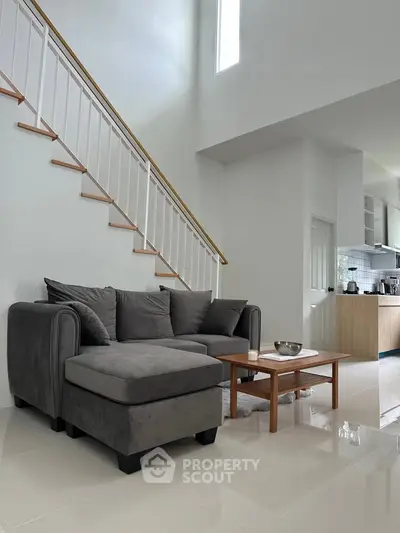 Modern living room with gray sectional sofa and open kitchen under staircase