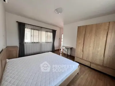 Spacious bedroom with wooden furniture and large window for natural light.