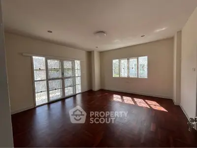 Spacious sunlit living room with elegant wooden flooring and large windows.