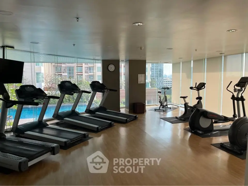 Spacious modern gym with treadmills and exercise bikes overlooking pool area.