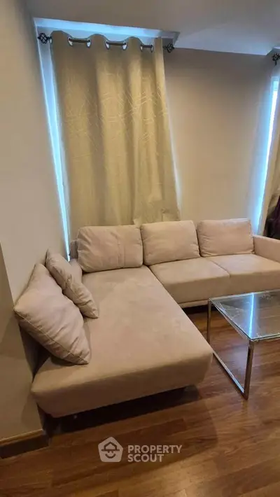 Cozy living room with beige sectional sofa and modern glass coffee table, perfect for relaxation.