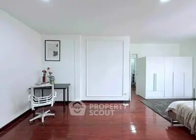 Spacious bedroom with modern decor and wooden flooring, featuring a study desk and large wardrobe.