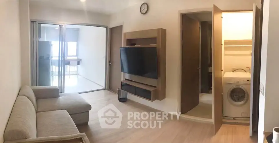 Modern living room with sleek TV setup and laundry area, featuring a cozy sofa and wooden flooring.