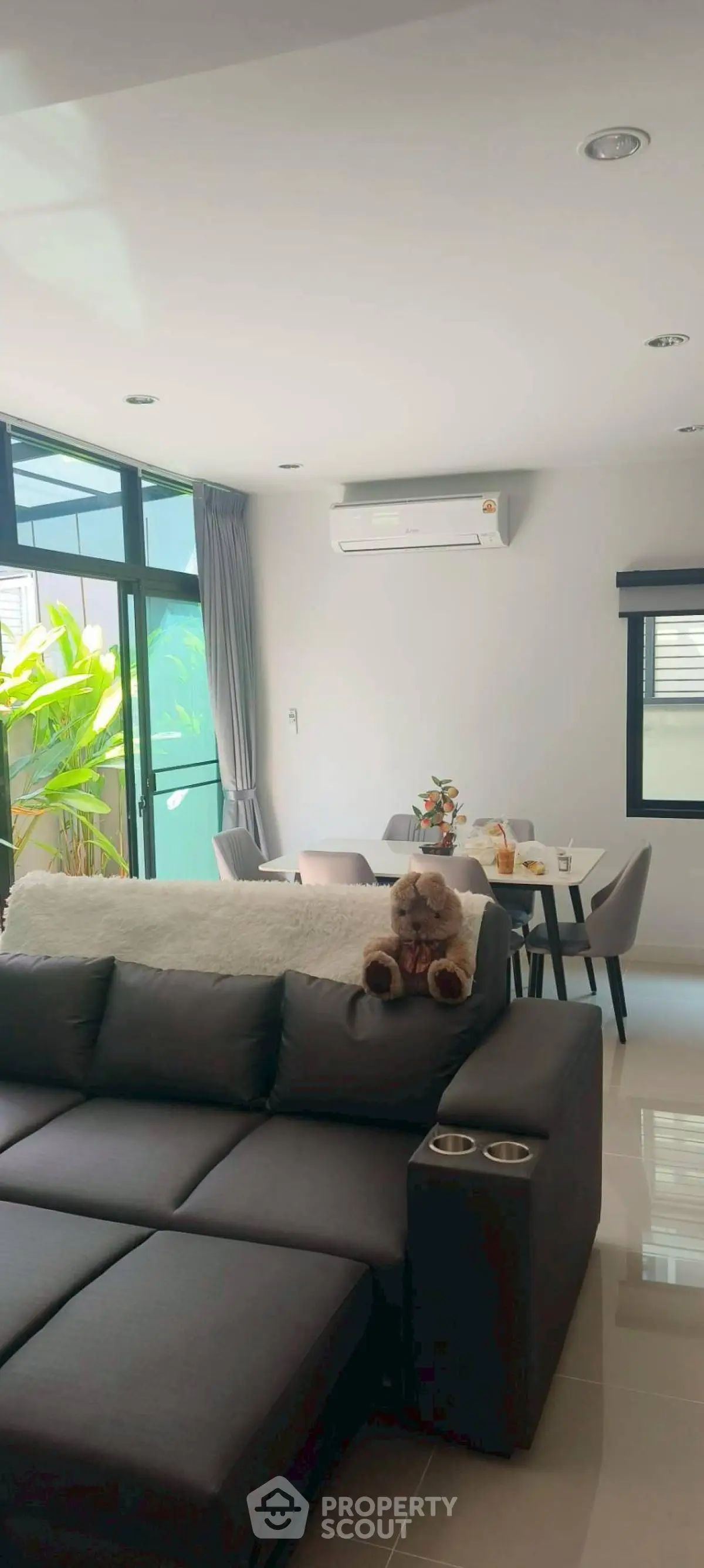 Modern living room with plush sofa and dining area, featuring large windows and natural light.