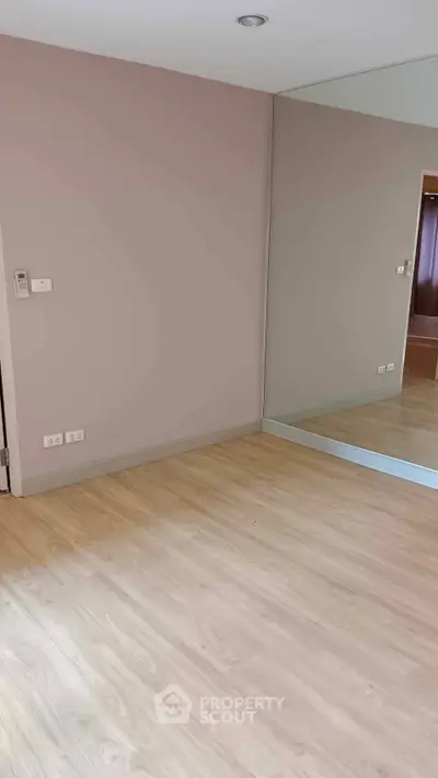 Spacious empty room with wooden flooring and large mirror, perfect for customization.