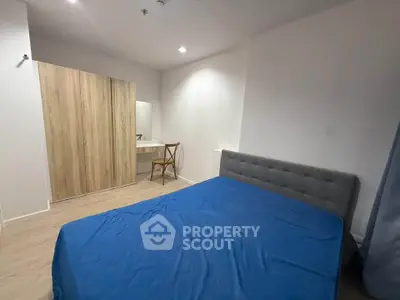 Modern bedroom with blue bedding, wooden wardrobe, and a stylish chair in a cozy apartment.