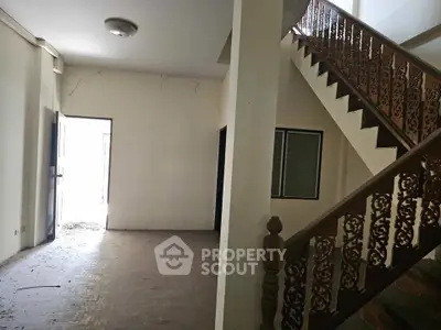 Spacious interior with ornate staircase and natural light, ideal for renovation.