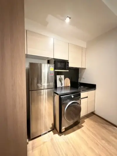 Modern kitchen with sleek appliances and wooden cabinetry, featuring a stainless steel fridge and washing machine.