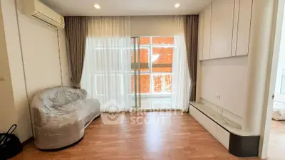 Modern living room with large window and air conditioning, featuring a wrapped sofa and sleek cabinetry.