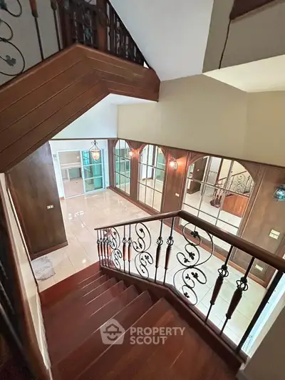 Elegant staircase with ornate railing leading to spacious living area with large windows.