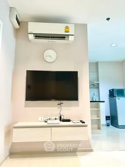 Modern living room with wall-mounted TV and air conditioning, adjacent to a sleek kitchen area.