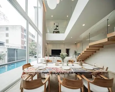 Luxurious open-plan living and dining area with pool view, modern staircase, and elegant decor.