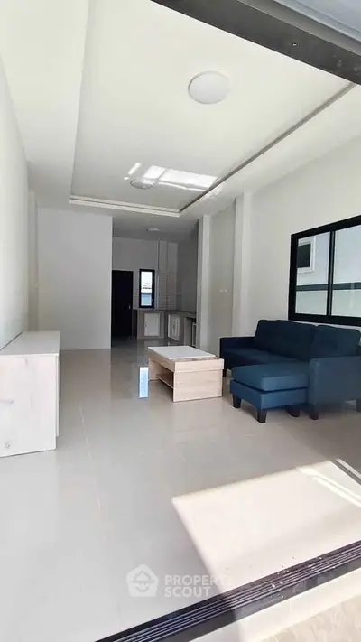 Modern living room with sleek furniture and open layout, featuring a blue sofa and natural light.