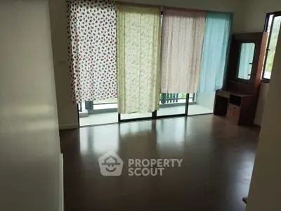 Spacious bedroom with large windows and wooden flooring, featuring a dresser and balcony access.