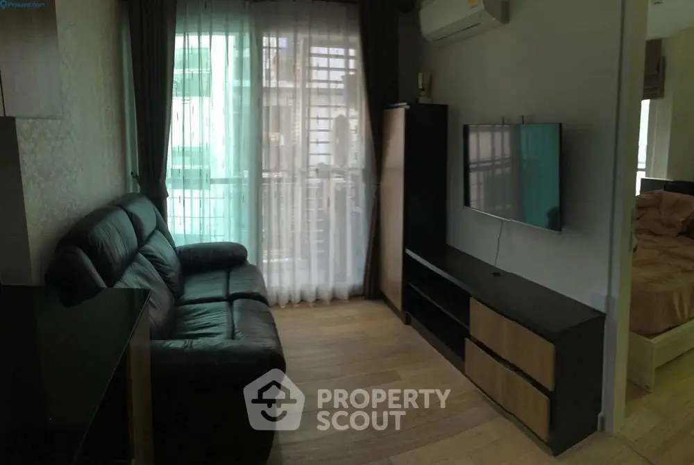 Modern living room with leather sofa, wall-mounted TV, and large window with sheer curtains.