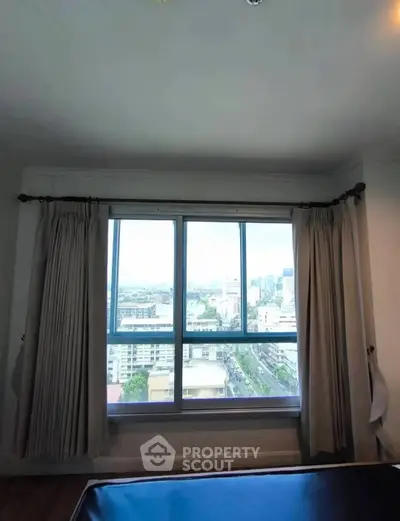 Spacious bedroom with large window offering stunning city views in high-rise apartment.