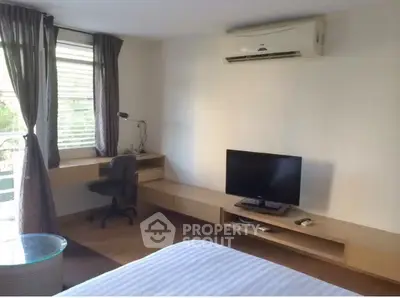 Modern bedroom with air conditioning and TV, featuring a sleek desk and large window for natural light.