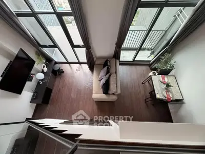 Modern living room with high ceiling and large windows offering city views.