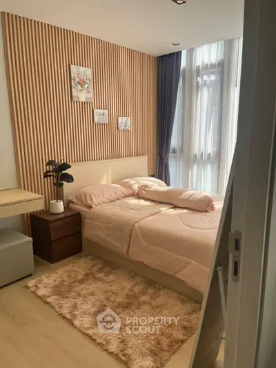 Cozy bedroom with modern decor, featuring a plush rug and natural light from large windows.