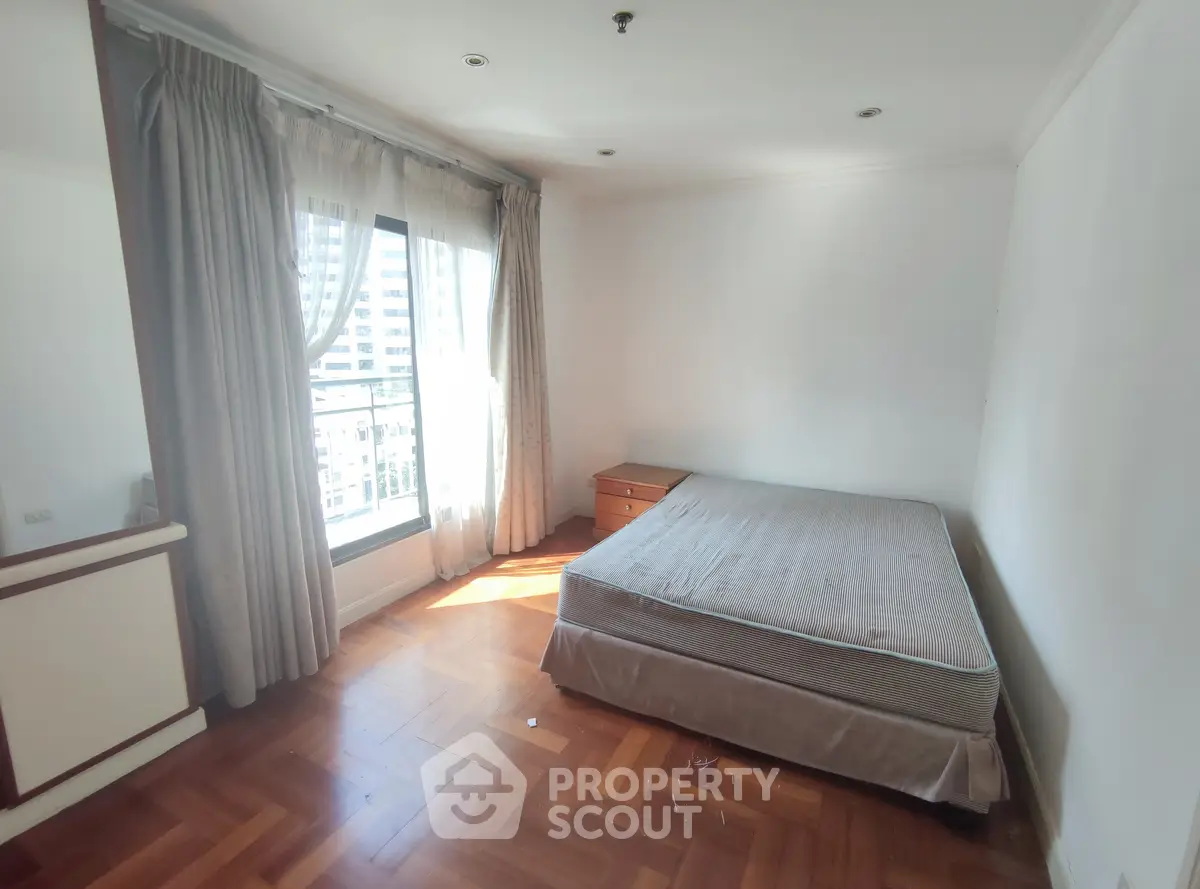 Bright bedroom with large window and parquet flooring in urban apartment