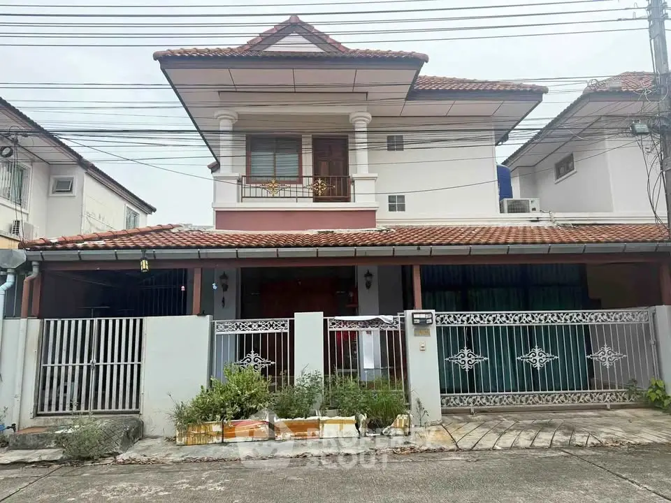 Charming two-story house with tiled roof and gated entrance in a suburban neighborhood.