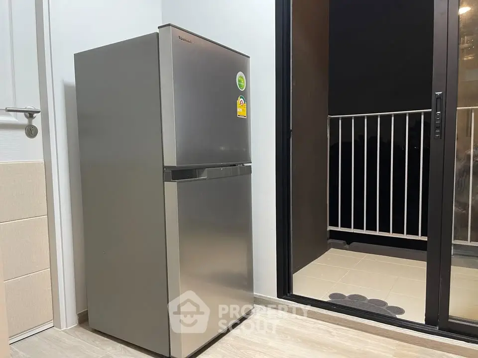 Modern kitchen corner with sleek refrigerator and balcony access, perfect for urban living.