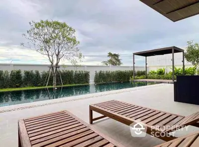 Luxurious outdoor pool area with wooden loungers and lush greenery, perfect for relaxation and leisure.