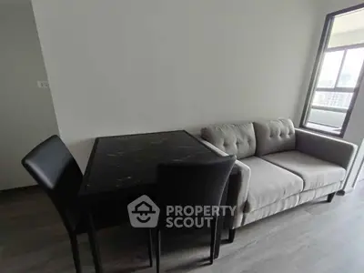 Modern living room with sleek sofa and dining table, featuring large window for natural light.