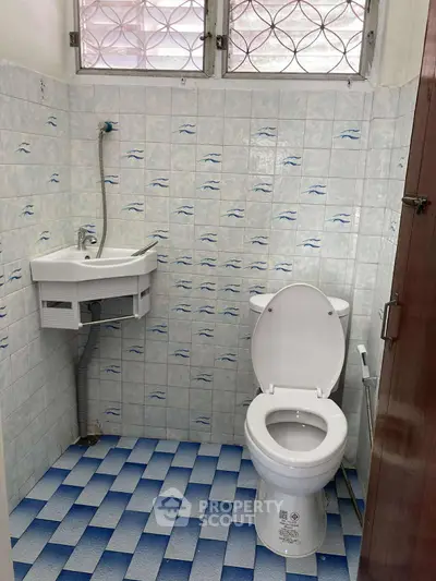 Compact bathroom with blue and white tiles, featuring a toilet and small sink.