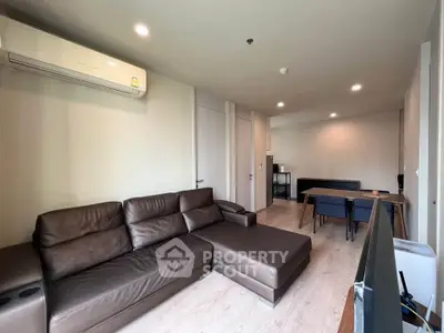 Modern living room with brown leather sofa and dining area in open layout apartment.