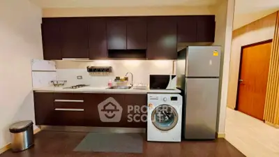 Modern kitchen with dark cabinets, washing machine, and stainless steel fridge in a cozy apartment.