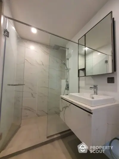 Modern bathroom with sleek glass shower enclosure, marble walls, and a stylish floating vanity sink, perfect for contemporary living.